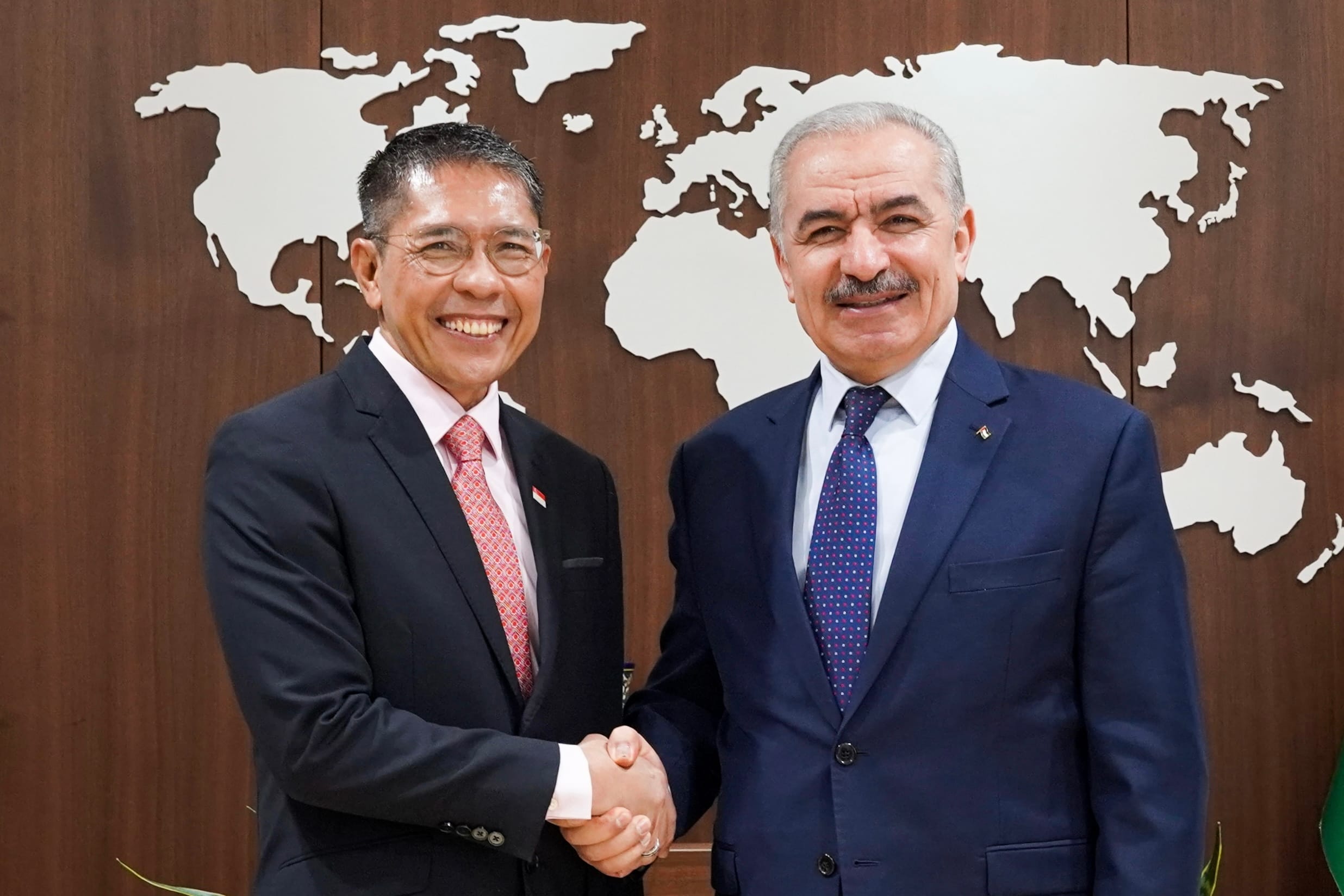 Two men in suits shaking hands in front of a world map.